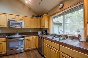 A kitchen with wooden cabinets, stainless steel appliances, a large window, and a view of the outdoors.