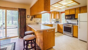 A kitchen with wooden cabinets, a central island with stools, a microwave, stove, and a refrigerator. - Rogue 16 (Bend)