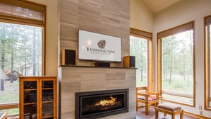 A modern living room with a fireplace, a mounted television, and a large window offering a view of the outdoors. - Rogue 16 (Bend)