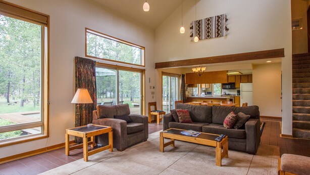 A spacious living room with a large window, a sofa, a coffee table, and a kitchen in the background. - Rogue 16 (Bend)