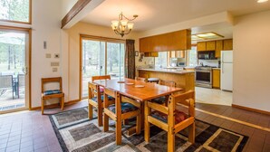 A dining area with a wooden table and chairs, a chandelier, and a view of the kitchen. - Rogue 16 (Bend)