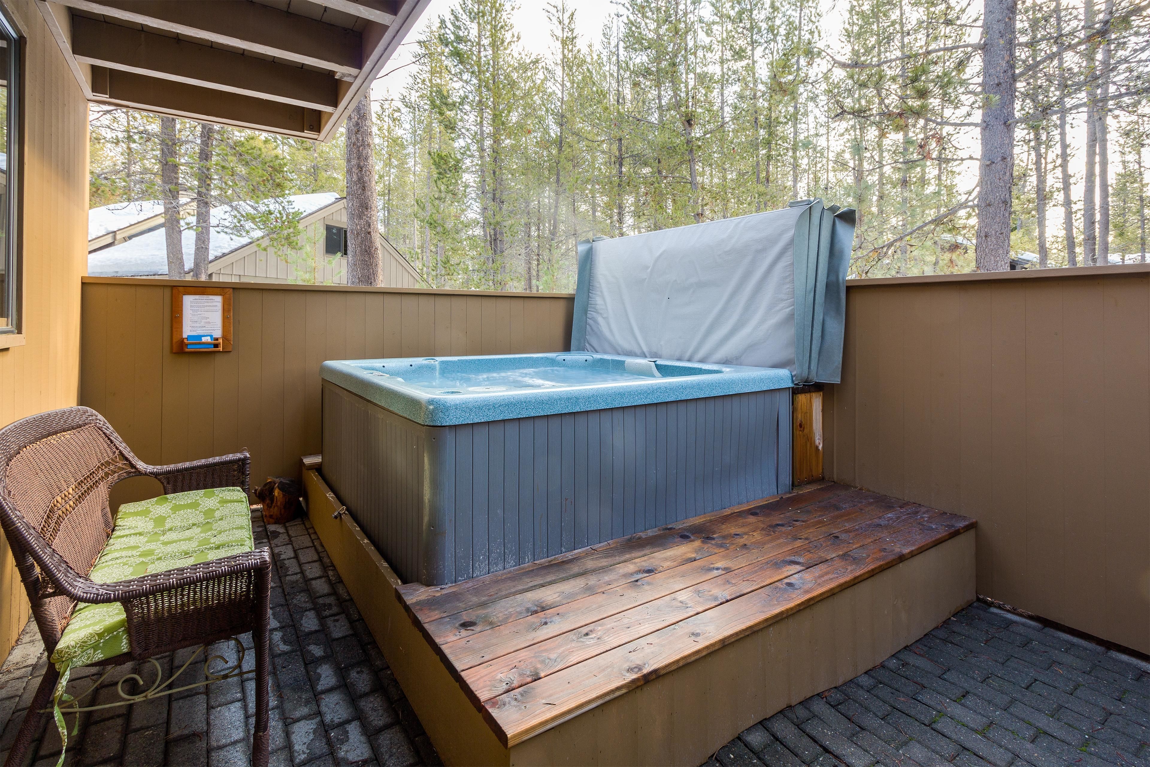 A hot tub with a wooden deck and a wicker chair.