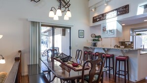 Uma sala de jantar com uma mesa de madeira comprida, cadeiras e um espaço de bar com banquetas.