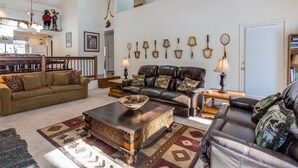 Uma sala de estar ampla com teto alto, área de jantar e escada para um andar superior.