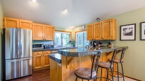 A kitchen with wooden cabinets, a stainless steel refrigerator, a granite countertop, and a bar area with stools. - Splitrock 11 (Bend)