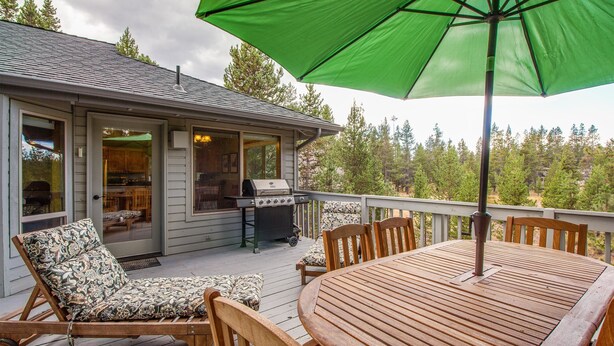 A wooden deck with a table and chairs, a grill, and a covered area with a green umbrella. - Splitrock 11 (Bend)