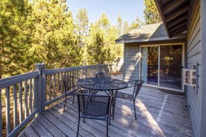 A wooden deck with a round table and chairs, a small building with a sliding glass door, and a wooden fence. - Splitrock 13 (Bend)