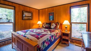 Un dormitorio con paneles de madera, una cama grande, dos lámparas de noche, un cuadro en la pared y una ventana con vistas a árboles.