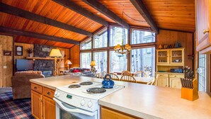 Una cocina amplia con una isla grande, armarios de madera y estufa integrada. Hay un comedor con mesa y sillas, y una sala de estar acogedora con sofá y chimenea.