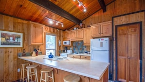 Cocina de cabaña de madera con una isla grande, taburetes de bar, microondas, refrigerador y piso con estampado de cuadros.