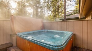 Un jacuzzi con revestimiento de madera, rodeado por una terraza de madera y una valla blanca.