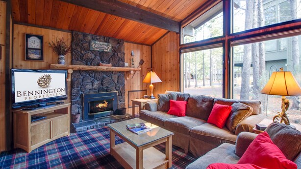 Interior acogedor de una cabaña con chimenea, paredes de madera, un sofá con cojines rojos y un televisor mostrando 'BENNINGTON PROPERTIES'.