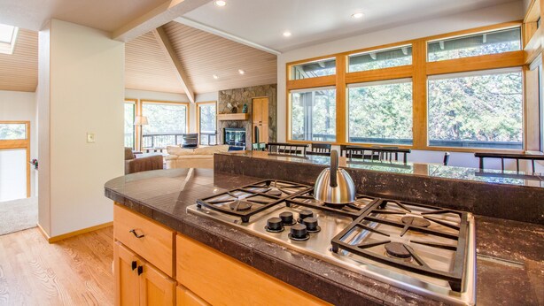 A modern kitchen with a gas stove, wooden cabinets, and large windows offering a view of the outdoors. - Sumac 9 (Bend)
