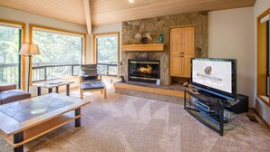 A spacious living room with a stone fireplace, a television, and a comfortable seating area with a view of the outdoors. - Sumac 9 (Bend)