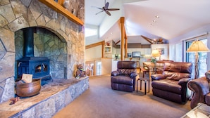 A spacious living area with a stone fireplace, leather chairs, and a dining table. - Tan Oak 15 (Bend)