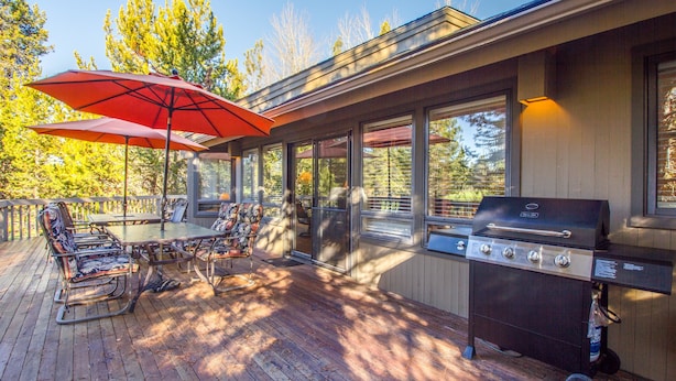 An outdoor patio with a grill, dining table, chairs, and a red umbrella. - Tan Oak 15 (Bend)
