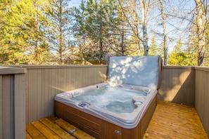 A hot tub with a wooden deck and a wooden fence, surrounded by trees.