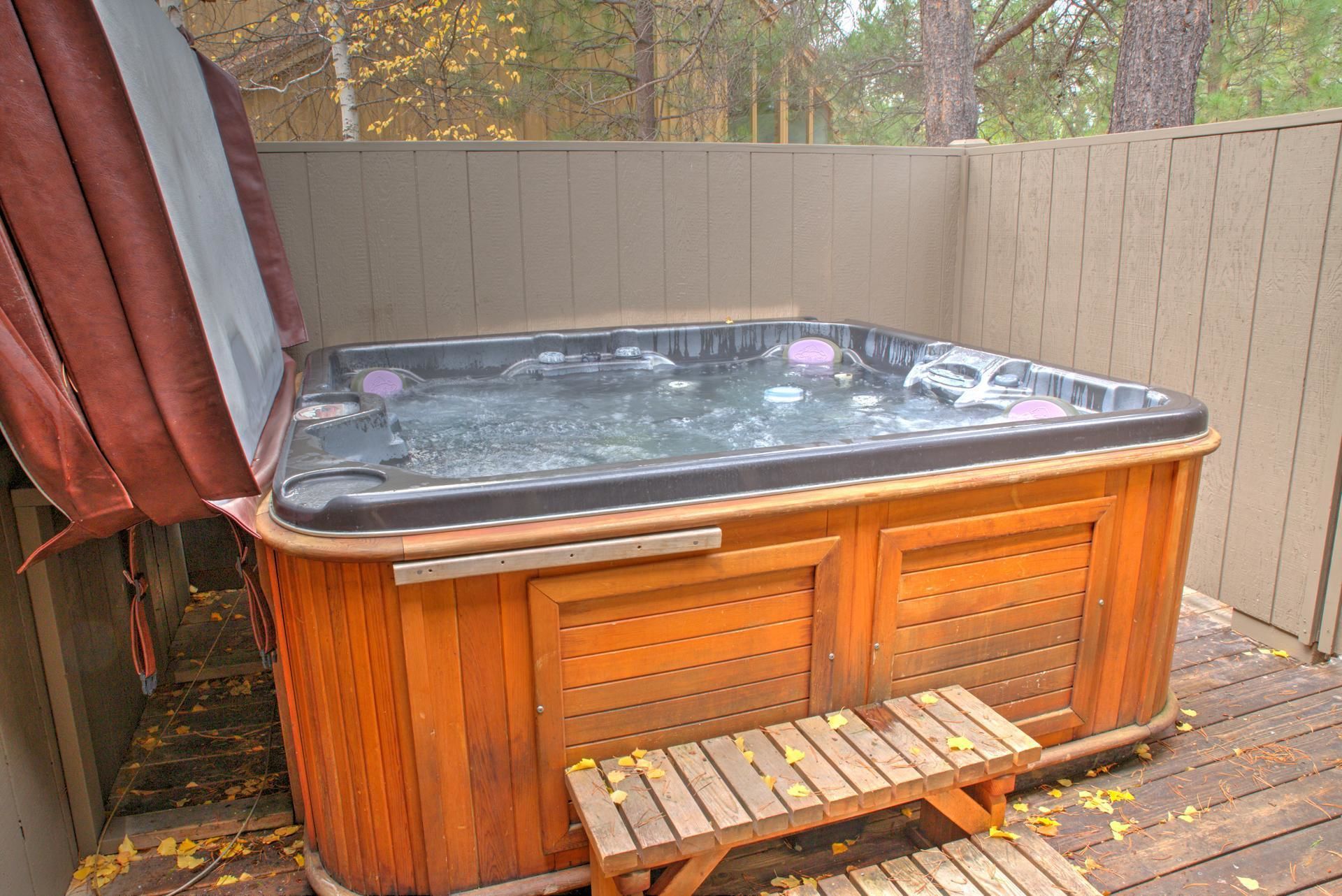 A wooden hot tub with a bench in front, surrounded by a wooden deck and a wooden fence.