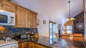 Una cocina con armarios de madera, encimera de granito, microondas, hervidor, tostadora y una zona de comedor con mesa y sillas.