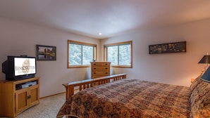 A bedroom with a large bed, a dresser, a television, and two windows.