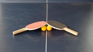 Two table tennis paddles and two balls on a dark table tennis table.