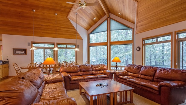 A spacious living room with leather sofas, a wooden coffee table, and large windows offering a view of the forest.
