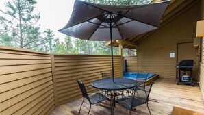 Une terrasse en bois avec une table et des chaises, un jacuzzi et un barbecue.