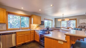A modern kitchen with wooden cabinets, a stainless steel dishwasher, a gas stove, and a large island with seating. - Topflite 12 (Bend)