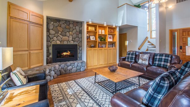 A spacious living room with a fireplace, wooden cabinets, a stone wall, a ceiling fan, and a cozy seating area. - Topflite 12 (Bend)