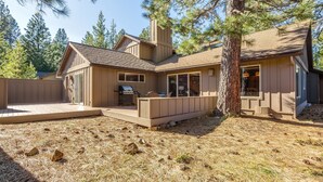 A two-story house with a deck, a chimney, and a large tree in front. - Topflite 12 (Bend)