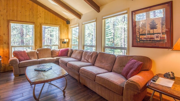 A cozy living room with a large sectional sofa, a coffee table, and large windows offering a view of trees. - Tumalo 11 (Bend)