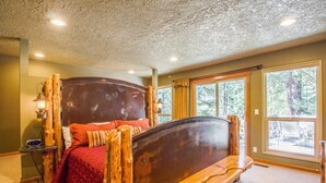 A bedroom with a wooden bed frame, a red quilt, and a nightstand with a lamp. - Tumalo 11 (Bend)
