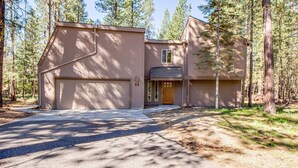 A two-story house with a garage, surrounded by tall trees. - Tumalo 11 (Bend)