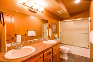 A bathroom with a double sink, a toilet, and a shower.