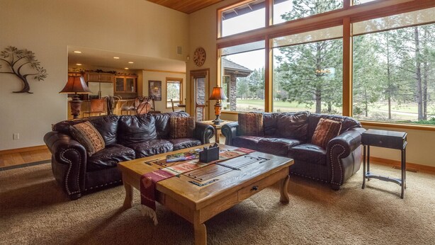 A spacious living room with two leather sofas, a wooden coffee table, and large windows offering a view of the outdoors. - Vista 16 (Bend)