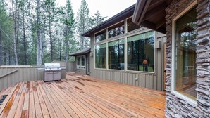 A wooden deck with a grill and stone wall, surrounded by trees. - Vista 16 (Bend)