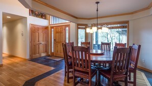 A dining area with a wooden table and chairs, a chandelier, and large windows. - Vista 16 (Bend)