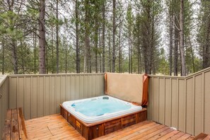 Un bain à remous sur une terrasse en bois, entouré d’une clôture en bois, avec une forêt en arrière-plan.