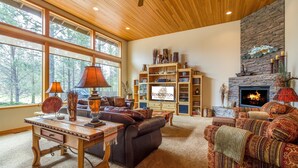 A spacious living room with a fireplace, large windows, and a stone accent wall. - Vista 16 (Bend)