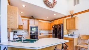 A kitchen with wooden cabinets, a central island with bar stools, a refrigerator, and a stove. - Warbler 12 (Bend)