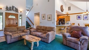 A spacious living room with two sofas and a coffee table, a staircase, and a kitchen area. - Warbler 12 (Bend)