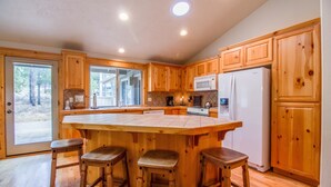 A spacious kitchen with wooden cabinets, a large island with stools, a microwave, and a refrigerator. - Whistler 2 (Bend)