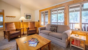 A cozy living room with a wooden coffee table, leather armchairs, a sofa, and large windows offering a view of the outdoors. - Whistler 2 (Bend)