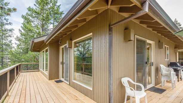 Una terraza de madera con una zona cubierta, ventanas amplias y mobiliario exterior.