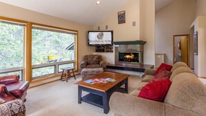 Amplia sala de estar con ventanas grandes, chimenea, televisor y asientos cómodos.