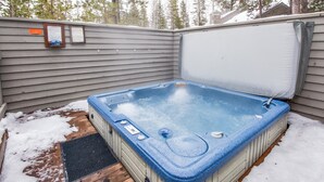Un bain à remous doté d’une terrasse en bois et d’un couvercle en métal, entouré de neige.