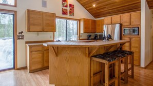 Une cuisine avec des meubles en bois, un grand îlot central doté de tabourets, un réfrigérateur et un four à micro-ondes.