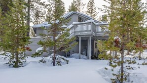 Une maison dotée d’un porche abrité et d’un toit recouvert de neige, entourée d’arbres.