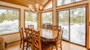 Un coin repas avec une table et des chaises en bois, de grandes fenêtres donnant sur un paysage enneigé et un plafond en bois.