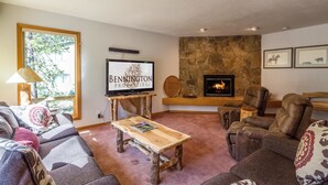 Una sala de estar acogedora con chimenea de piedra, asientos cómodos, televisión y un ventanal grande.
